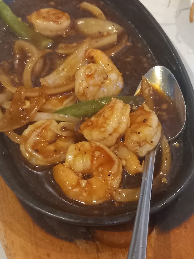 King prawns with onions and snap peas in dark sauce on a sizzling plate